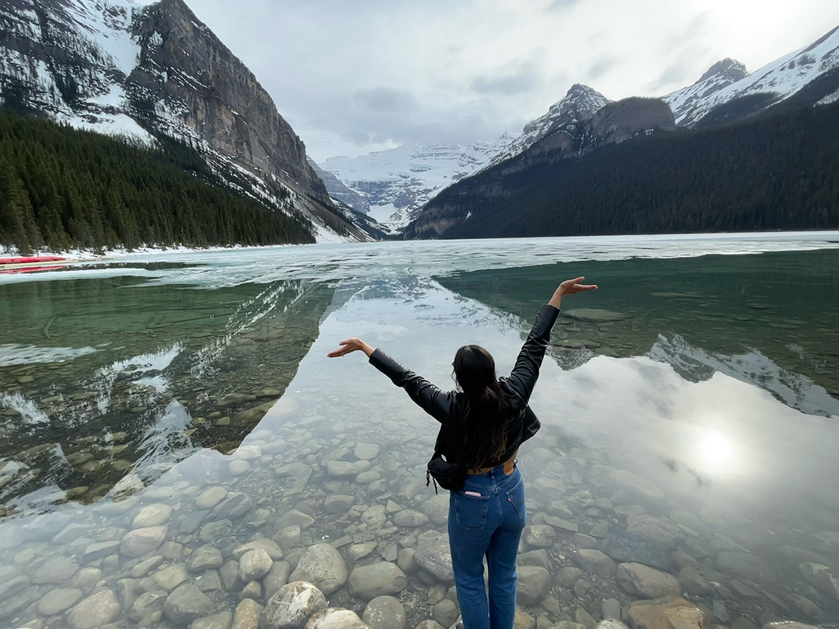 Affirm team member standing at the edge of a river with her arms raised looking at the mountains
