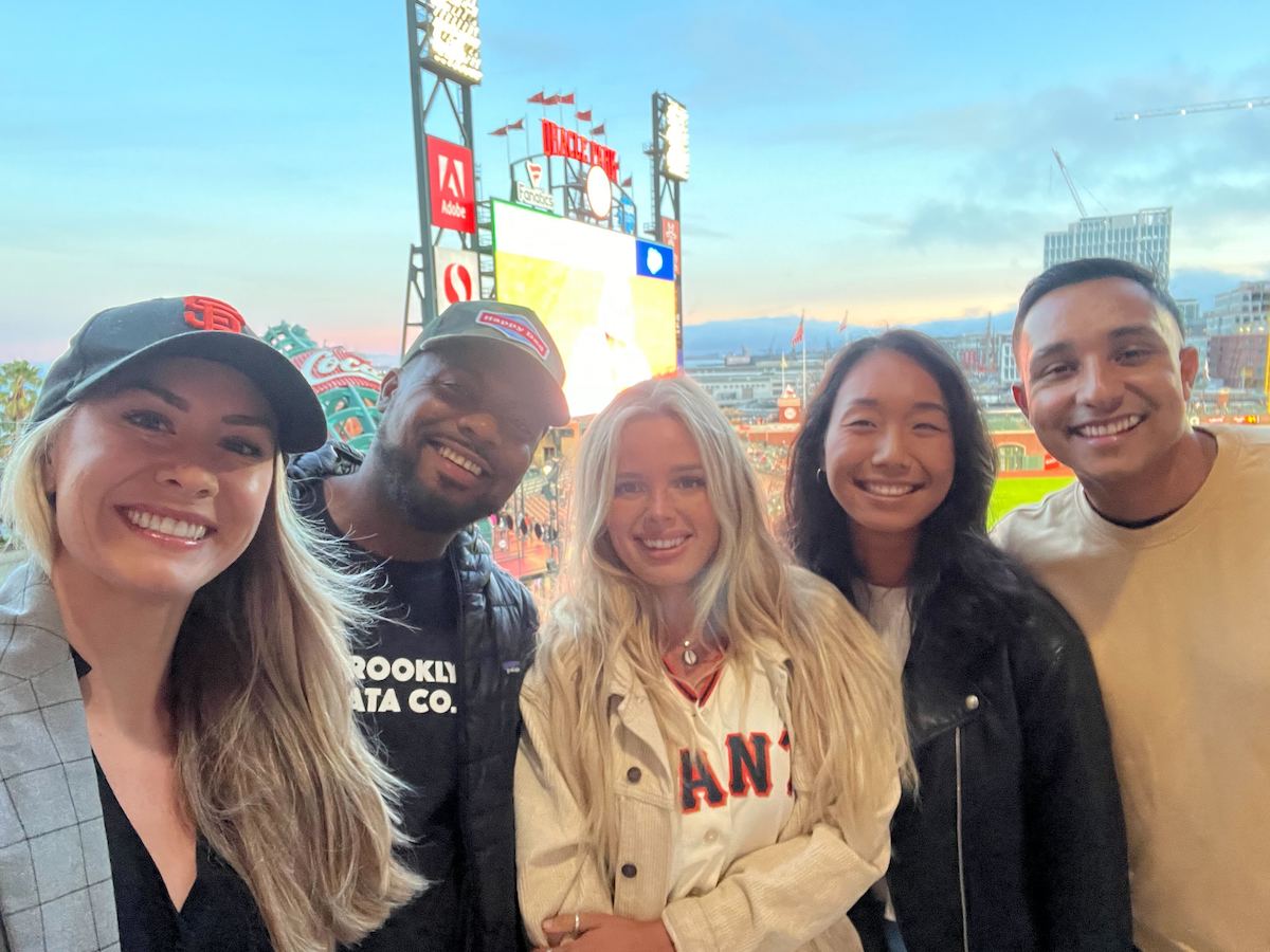 Five men and women smile at a baseball game