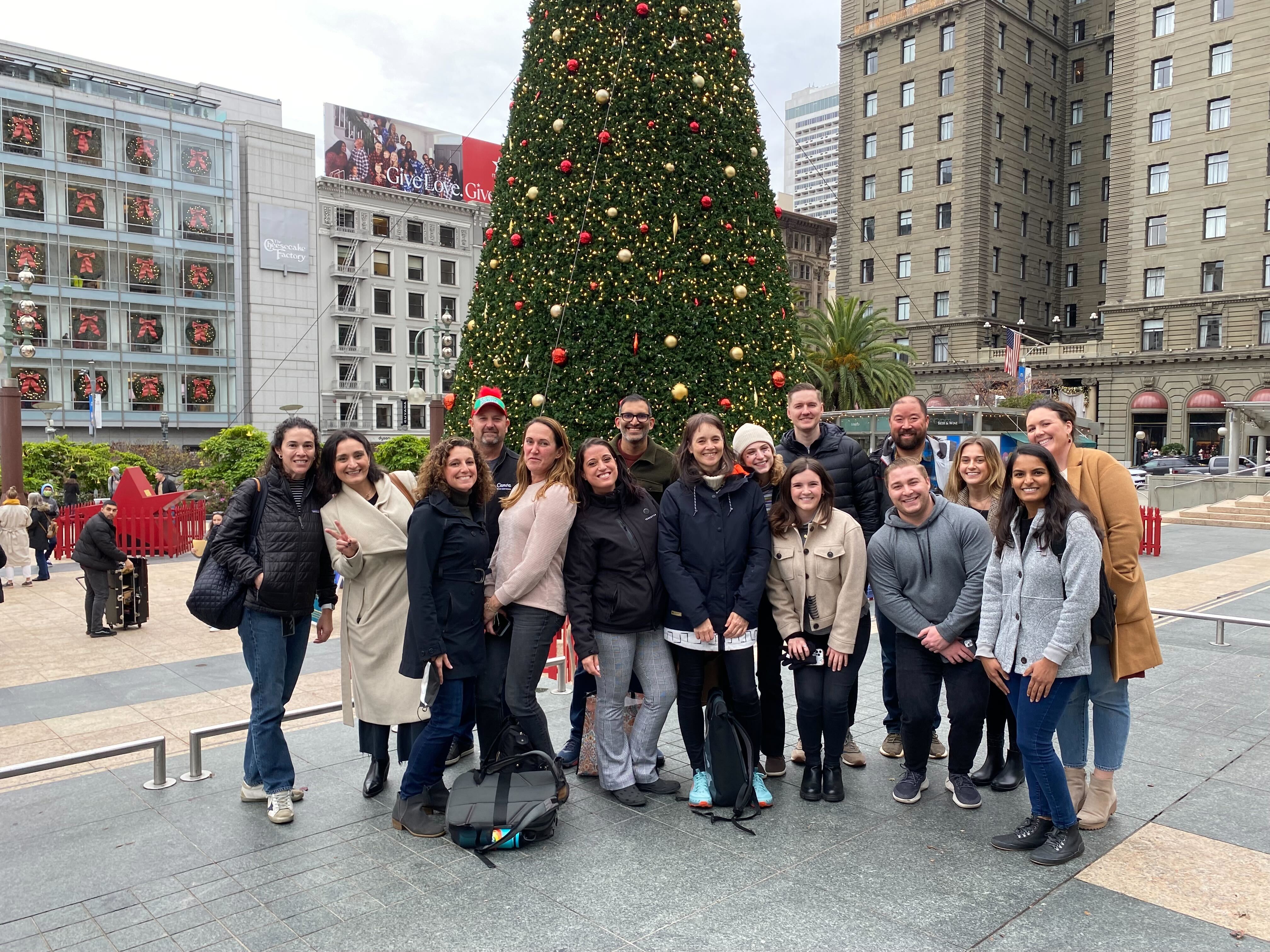 An image of Canva employees smiling in front of a Christmas tree. 