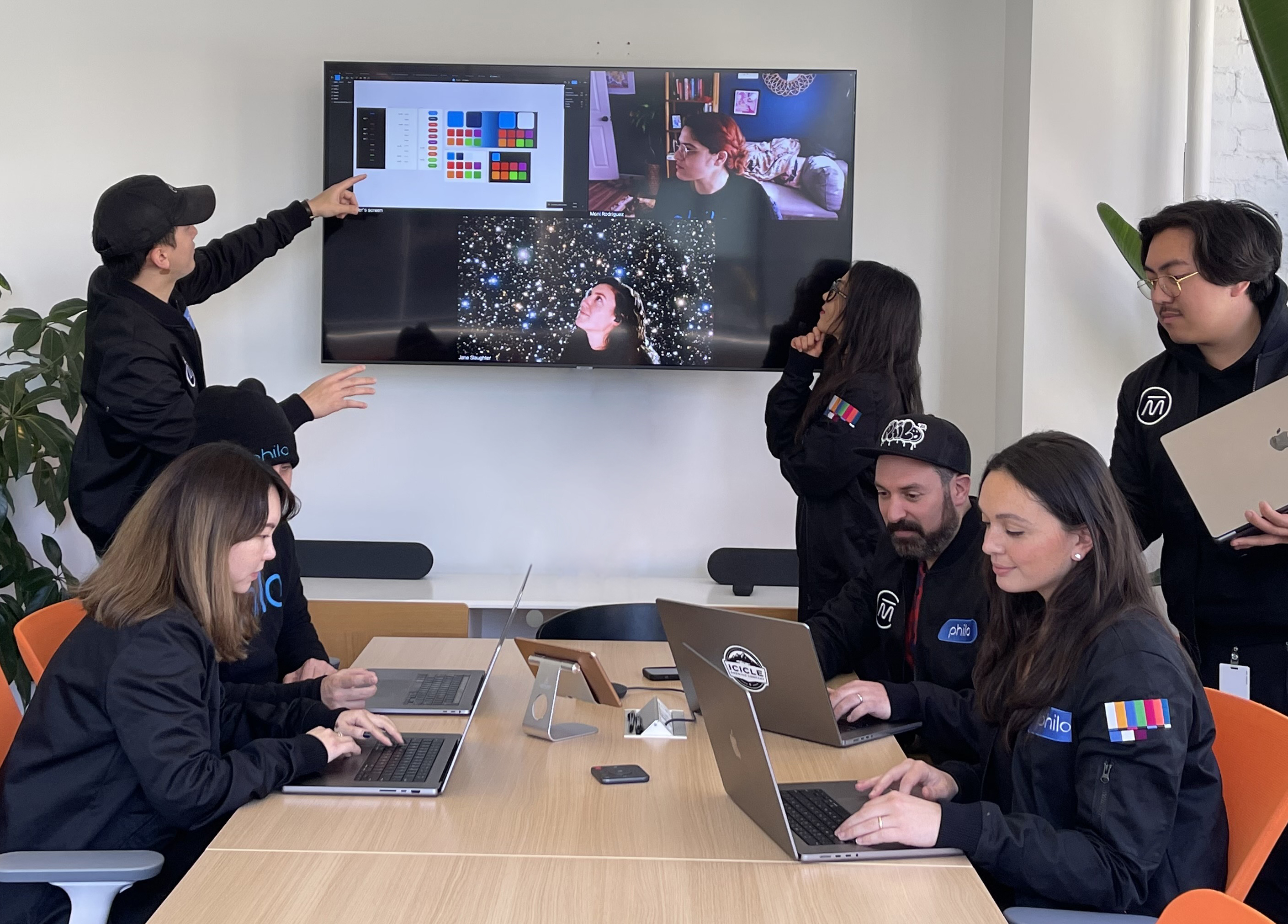 The Philo design team clusters in a conference room, pointing at a screen with two people featured