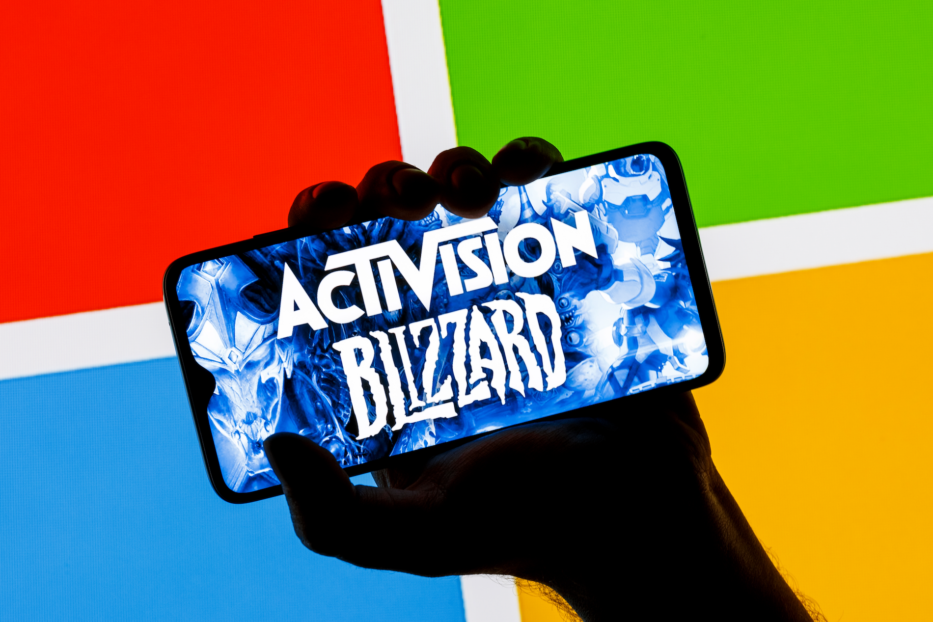 ctivision Blizzard logo on smartphone screen in hand against background of Microsoft logo. 