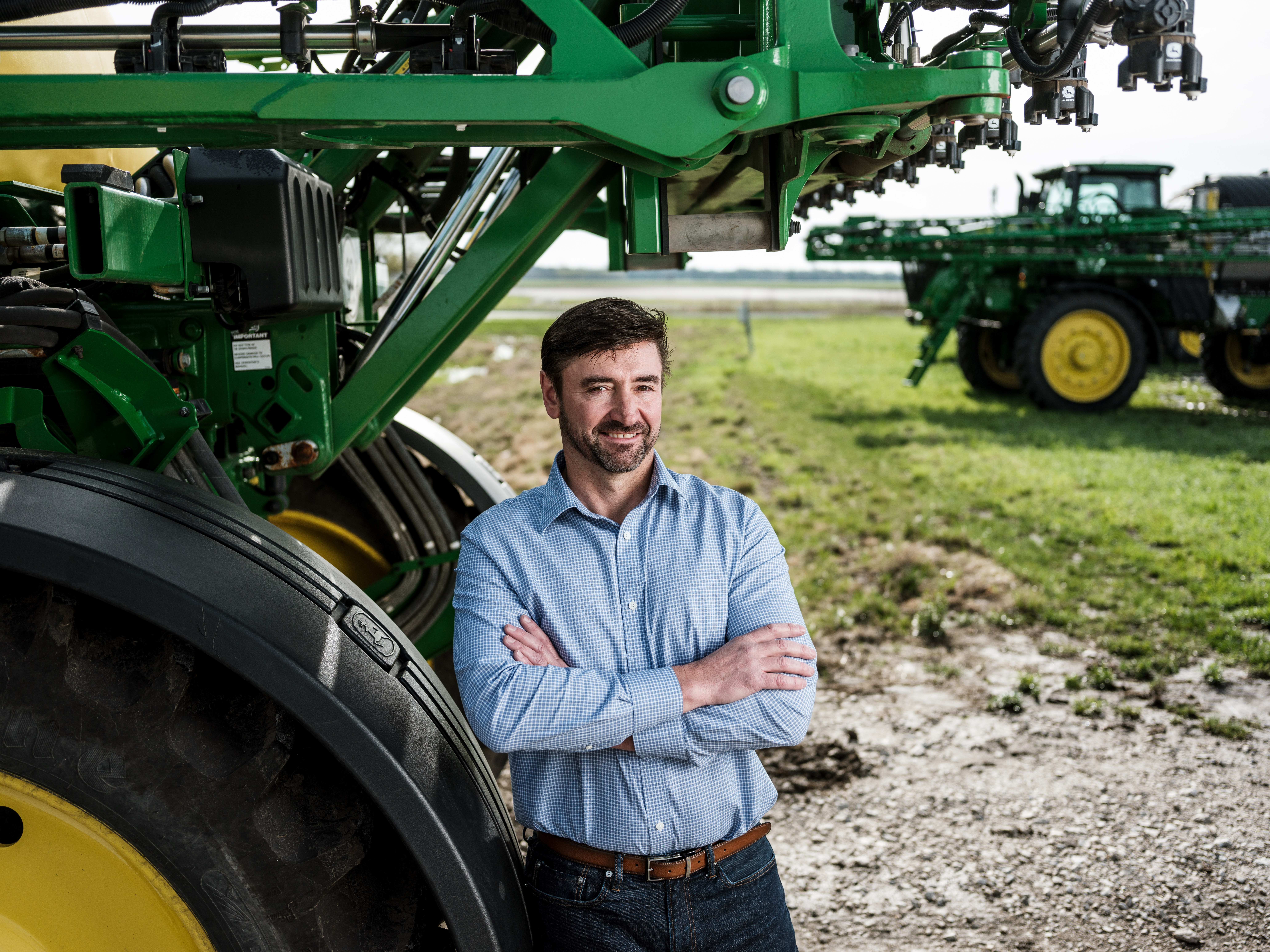 Portrait of Rich Humpal standing against the tire of a piece of John Deere equipment in a field.