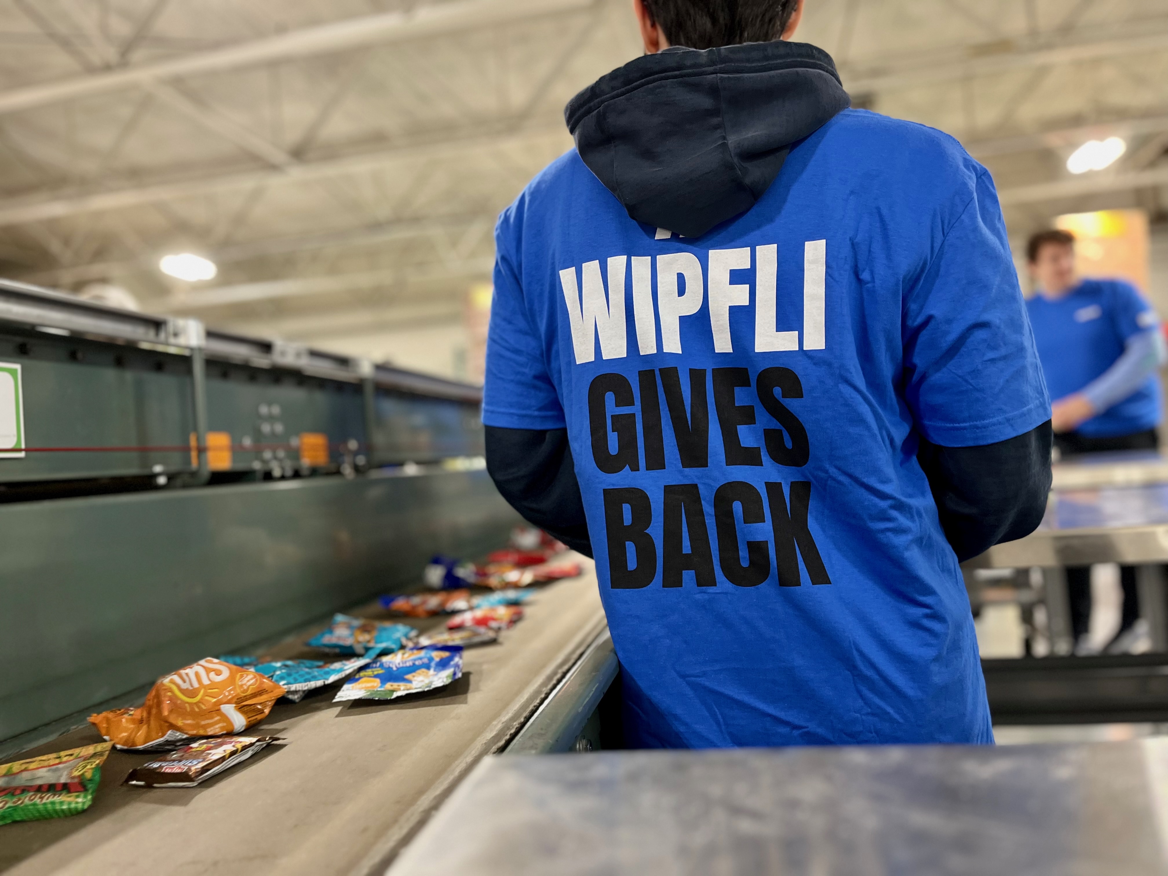 A team member faces away from the camera and wears a t-shirt that reads “Wipfli Gives Back” 