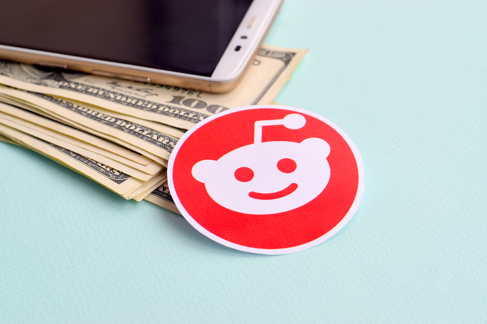 An image of a sticker with the Reddit logo sitting atop a pile of cash is shown.
