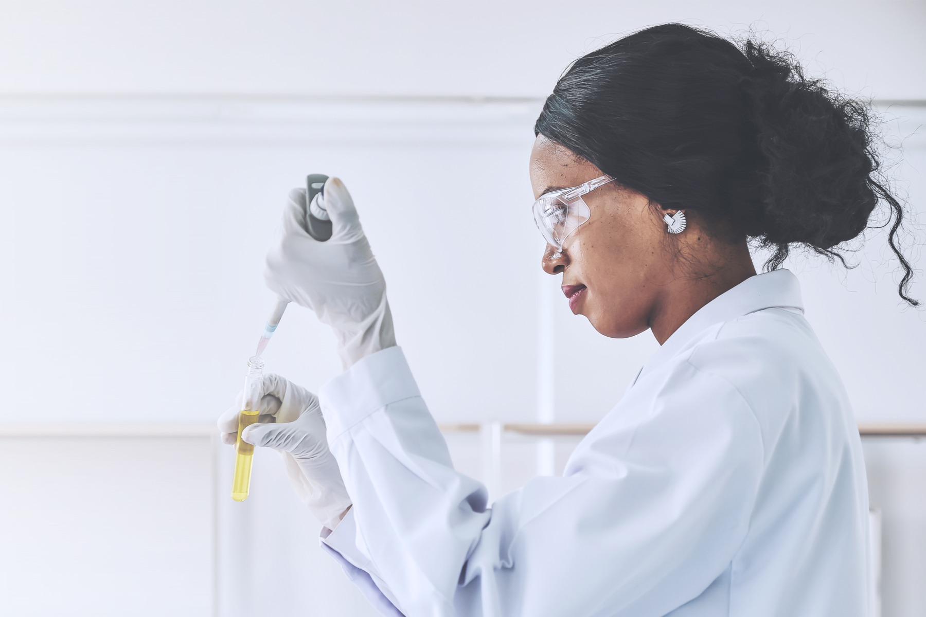Image of a woman scientist wearing a lab coat and conducting experiment with a dropper and test tubes  