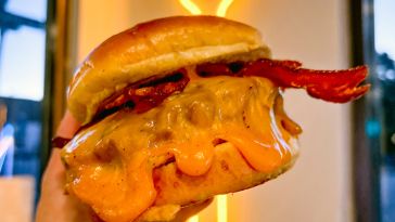 a gooey cheese burger held in front of a neon sign