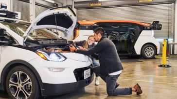 Two Cruise workers look under the hood of a vehicle in Cruise's garage