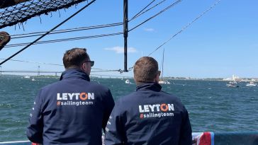 Two people with “Leyton #sailingteam” jackets face the ocean.