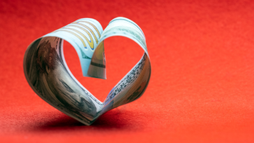 Photo of a $100 bill folded into a heart shape red background