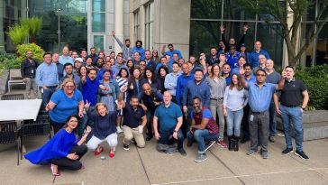 Warner Bros. Discovery team members post for group photo — all wearing blue — outside their Bellevue, Washington, office.