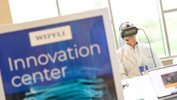Wipfli team member wearing VR headset behind sign that reads “Wipfli Innovation Center.”