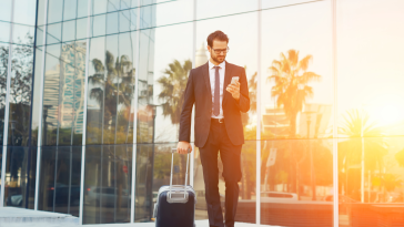 A man in a suit holding a phone and a suitcase is shown.